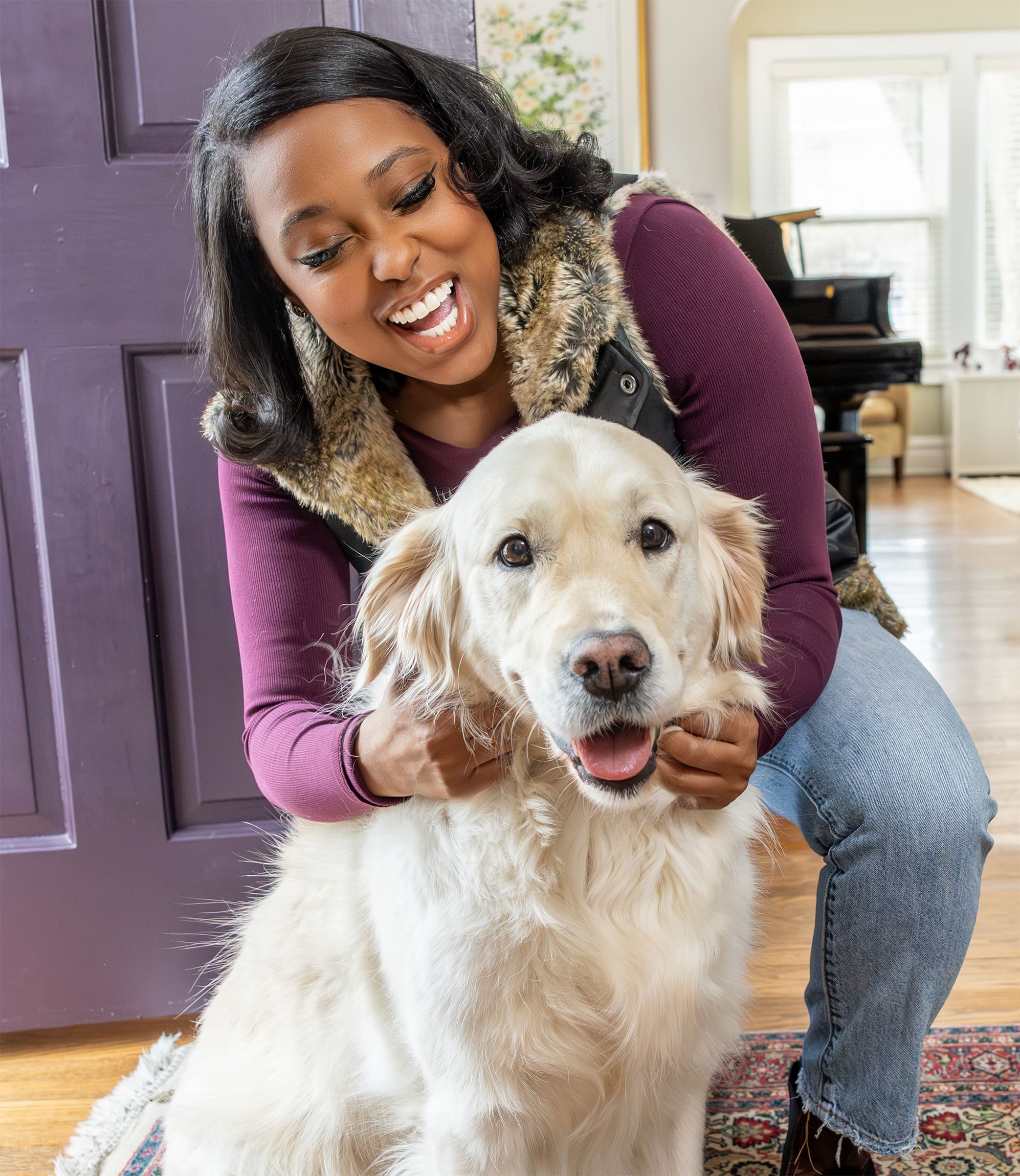 Shantel Franklin with a big smile petting a golden retriever in a house